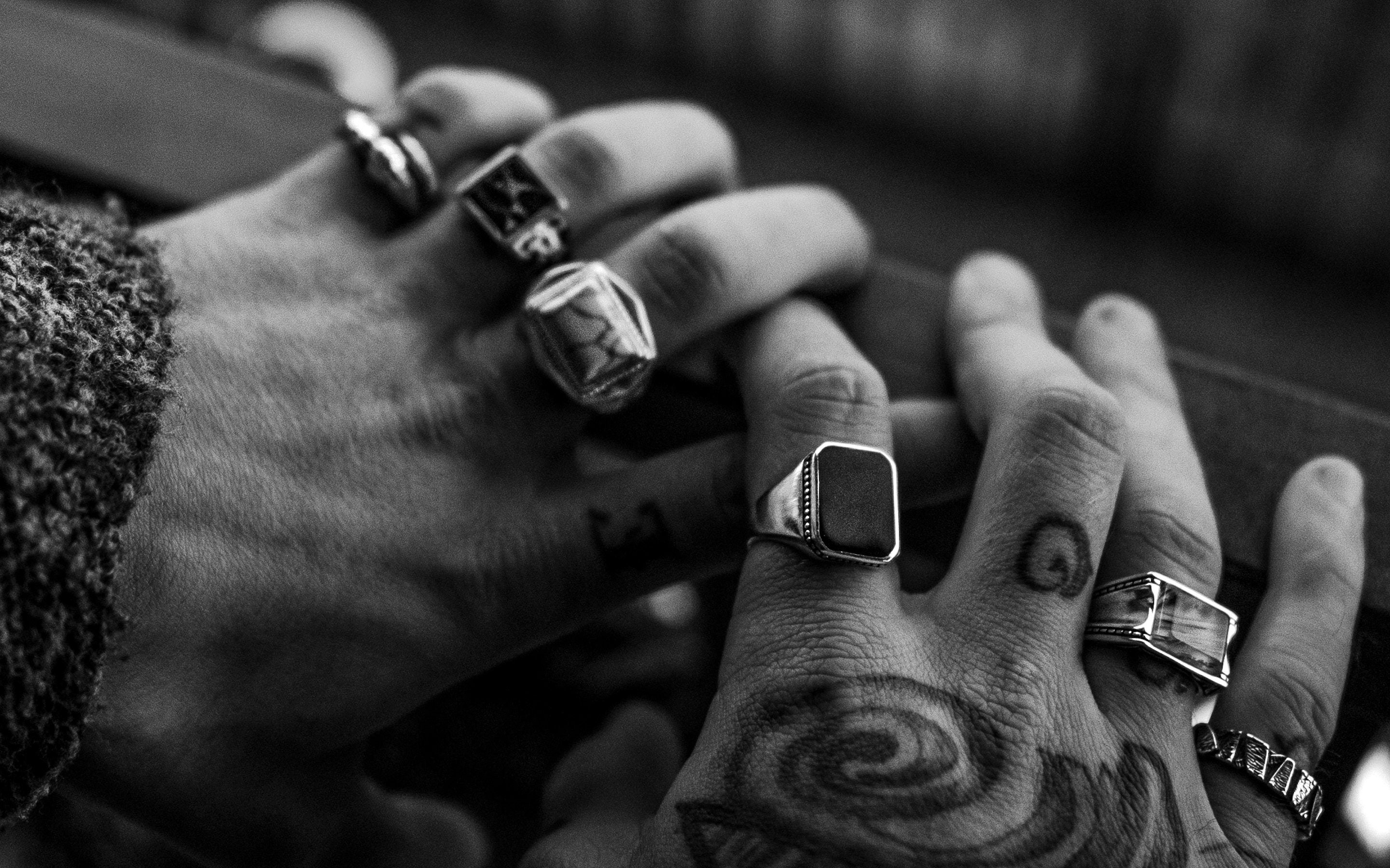 A black and white photo of tattooed hands holding rings.